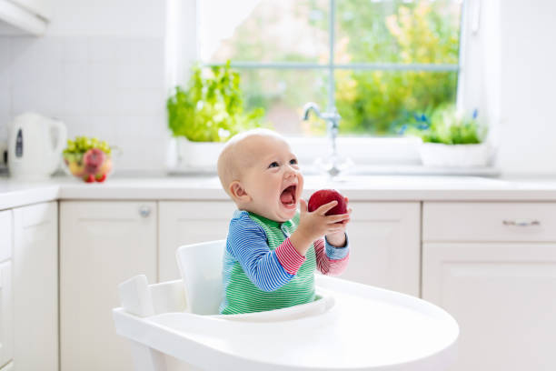 istock Baby boy eating apple in white kitchen at home 671751216