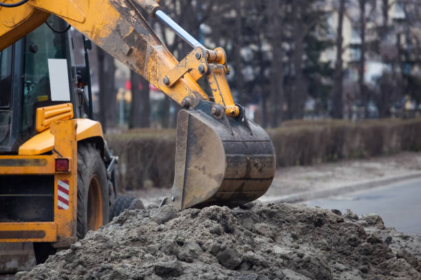 A large yellow excavator stands in the middle of the street A large yellow excavator stands in the middle of the street near the dug hole. backhoe photos stock pictures, royalty-free photos & images