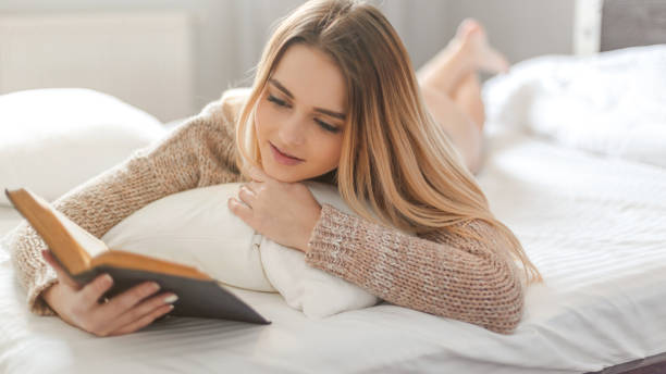 istock Happy woman enjoying in a book while relaxing in bed 671770772