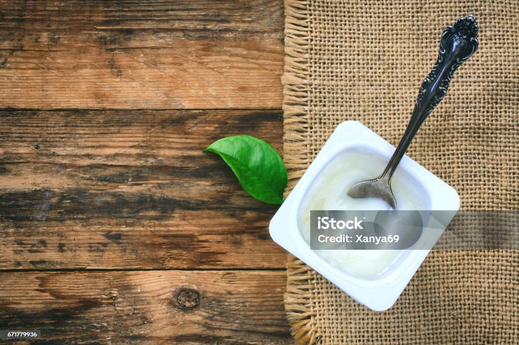 Yogurt in a plastic white container, vintage spoon Yogurt in a plastic white container, vintage spoon, green leaf, canvas napkin on a wooden table Jar Stock Photo