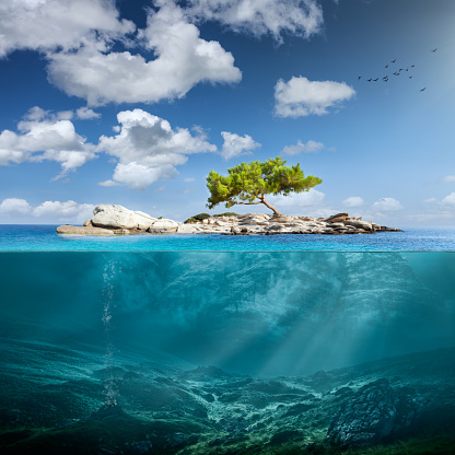 Beautiful underwater view of lone small island above and below the water surface in turquoise waters of tropical ocean.