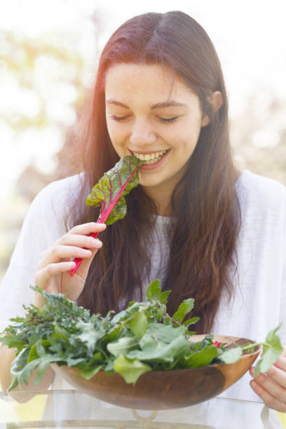 jovem mulher comendo uma folha de acelga vermelha rubi - ruby red chard fotos - fotografias e filmes do acervo