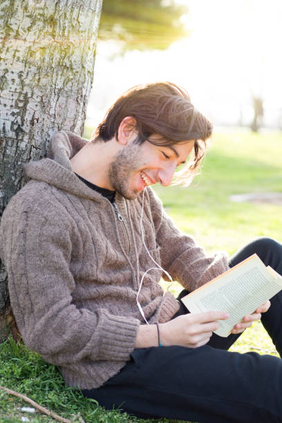 istock Young man reading book in the park 671838882