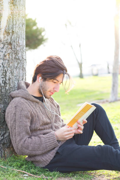 istock Young man reading book in the park 671839070