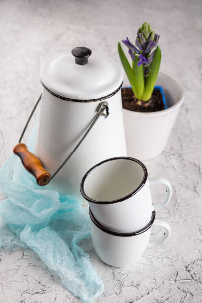 Vintage home arrangement, soft pastel colors. Two white enamel mugs, white can and blossoming flower hyacinth in pot on light background blue jug stock pictures, royalty-free photos & images