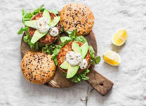 Fish burger. Burgers with tuna, avocado and mustard sauce with whole grain homemade buns on wooden cutting board on a light background, top view