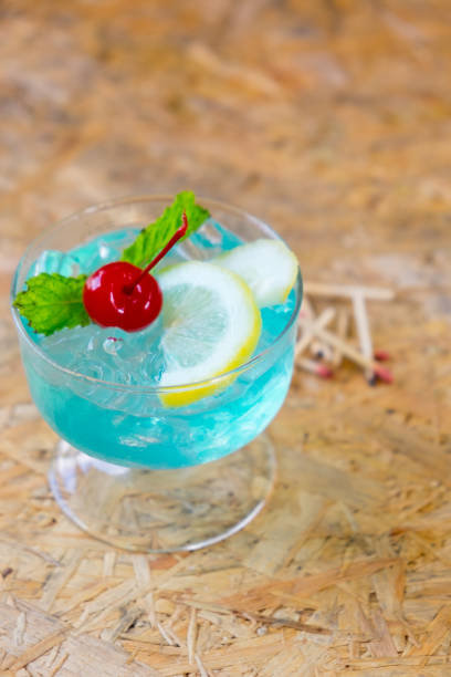 istock Blue cocktail with a slice of lemon, mint and cherry on wood table 671879404