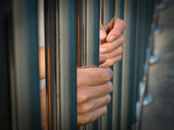 istock Hand of prisoner holding prison bars in jail. 671899478
