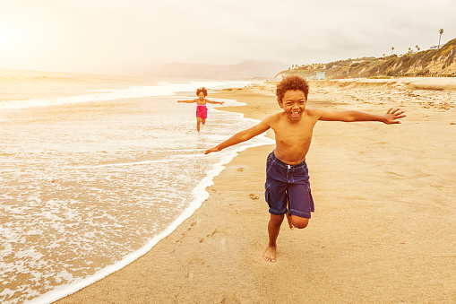 Photo of two young African American siblings running carefree on a California beach at sunset