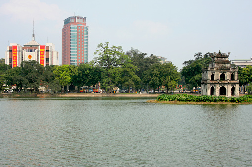 Hanoi, Vietnam - April 22 2009: Ngoc Son Temple on a small island on the Hoan Kiem Lake with behind, from left to right, the Hanoi Municipal People's Committee, the Vietcombank Tower and the dragons of the Statue of Ly Thai To.