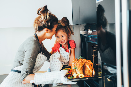 Little girl watching her mother taking the turkey out of the oven.