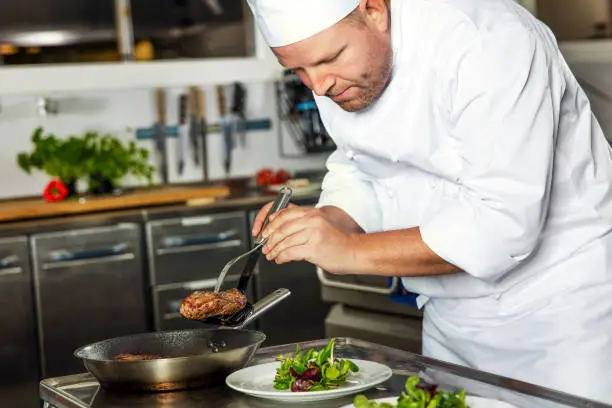 Photo of Focused chef prepares steak dish at gourmet restaurant