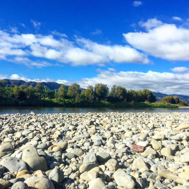 istock River Scene with river rocks in foreground, green trees on horizon with a blue sky and clouds 671951530