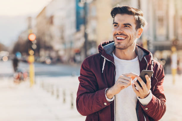 Young man with smart phone in the city Young man with smart phone texting outdoors in the city one young man only stock pictures, royalty-free photos & images