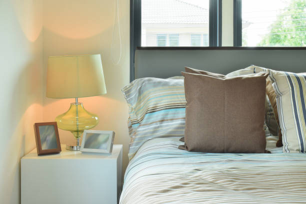 istock Brown pillow with striped bedding and green table lamp on white bed side table 671961836