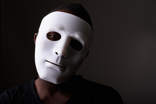 Studio shot of young black African man in dark room wearing mask horizontal shot