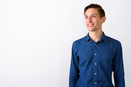 Studio shot of happy young handsome man smiling and thinking while looking up against white background horizontal shot