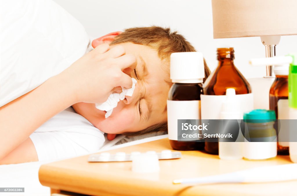 Sick kid boy with bad cold using paper napkins Close-up portrait of sick kid boy with bad cold laying in bed and using paper napkins 6-7 Years Stock Photo