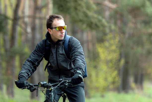 A medium close-up of a young man who is enjoying a bike ride in Northumberland in the North East of England he is pushing his bike and is taking the time to enjoy the surroundings and having some mindfulness he is looking up at the trees.