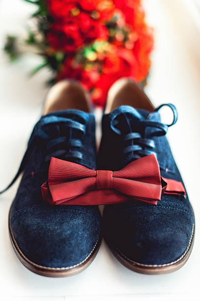 nahaufnahme des modernen menschen zubehör. cherry bow-tie, blau leder shoest und rote hochzeit bouquet auf einem teppich. - shoe groom wood luxury stock-fotos und bilder