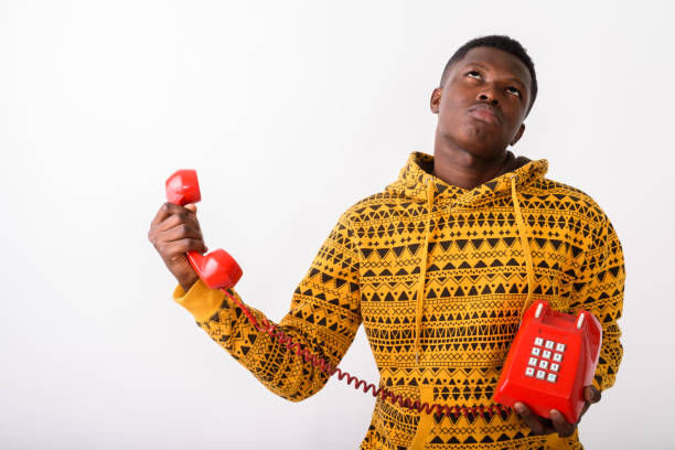istock Studio shot of young black African man holding old telephone while thinking and looking annoyed against white background 672040296