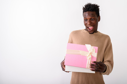Studio shot of young happy black African man smiling while opening gift box and looking shocked against white background horizontal shot
