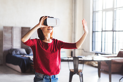 Happy young woman wearing VR Glasses in loft apartment