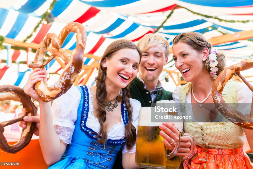 Friends with giant pretzels in Bavarian beer tent Three friends in beer tent at Dult or Beer Fest holding giant pretzels up in the air Beer Festival Stock Photo