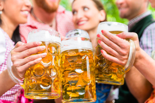 Friends having fun in beer garden while clinking glasses Five friends, men and women, having fun in beer garden clinking glasses with beer oktoberfest beer stock pictures, royalty-free photos & images