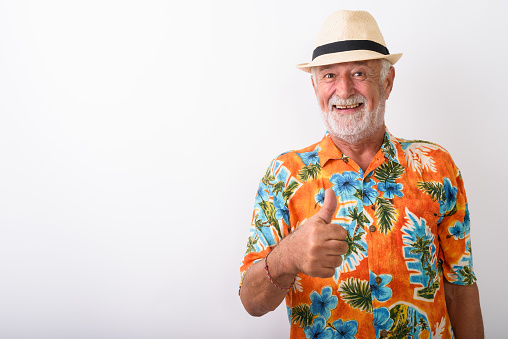 Studio shot of happy senior bearded tourist man smiling while giving thumb up and wearing hat against white background horizontal shot