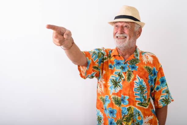 istock Studio shot of happy senior bearded tourist man smiling while pointing at distance while wearing hat against white background 672050556