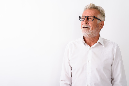 Studio shot of happy senior bearded man smiling and thinking with eyeglasses against white background horizontal shot