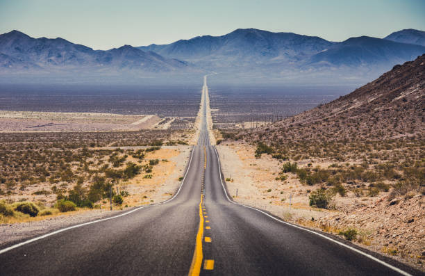Endless straight road in the American Southwest, USA Classic panorama view of an endless straight road running through the barren scenery of the American Southwest with extreme heat haze on a beautiful hot sunny day with blue sky in summer mojave desert stock pictures, royalty-free photos & images