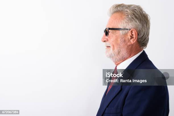 Ver Perfil De Feliz Senior Barbudo Hombre De Negocios Sonriendo Mientras Lleva Puesto Anteojos Contra Fondo Blanco Foto de stock y más banco de imágenes de Perfil - Vista de costado