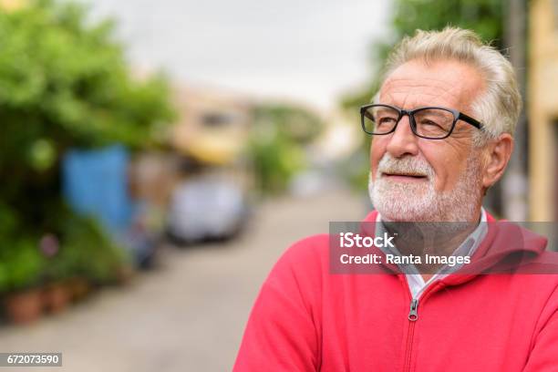 Close Up Of Happy Handsome Senior Bearded Man Smiling While Thinking And Looking Up With Eyeglasses Outdoors Stock Photo - Download Image Now