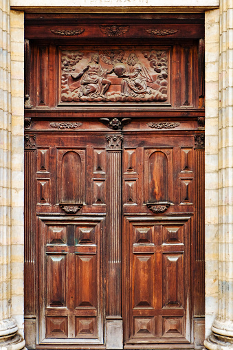 Above the main entrance a religious relief is carved into the wood, the entry itself is ornate with geometric shapes and other decorative ornaments. The door is rectangle and surrounded by stone columns.
