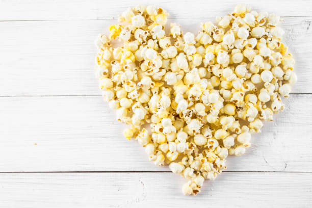 istock Salted popcorn in the shape of heart on a white table. Top view. 672084392