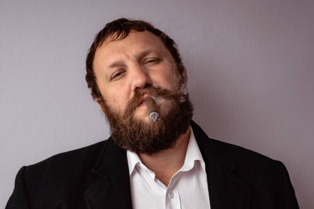 istock Bearded man in modern coat and shirt smoking his cigar. 672100154