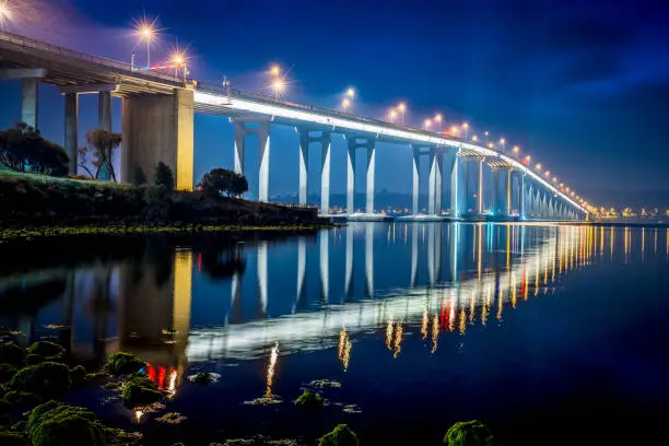 Famous Tasman Bridge crossing the Derwent River towards the City of Hobart at night. The illuminated bridge, on of the major icons - symbols of Hobart - mirroring in the calm Derwent River Water, Hobart, Tasmania, Australia.