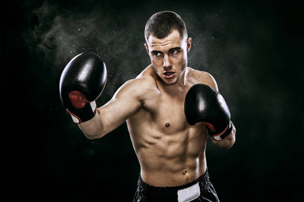 boxeur thaïlandais sportif muay combats dans les gants dans la cage de la boxe. isolé sur un fond noir avec de la fumée. copiez l’espace. - kick boxing photos et images de collection