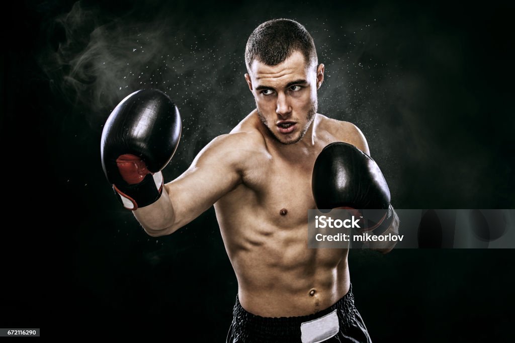 Sportsman muay thai boxer fighting in gloves in boxing cage. Isolated on black background with smoke. Copy Space. Street fighter fighting in boxing gloves. Isolated on black background with copy Space. Action shot. Sport concept. Boxing - Sport Stock Photo