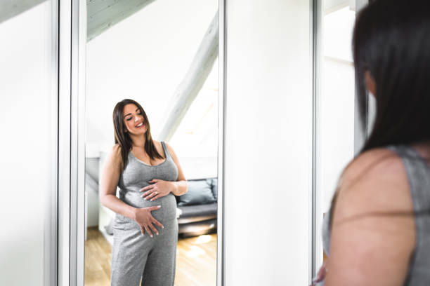 istock pregnant woman looking her self at the mirror 672123530