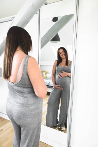 istock pregnant woman looking her self at the mirror 672123642