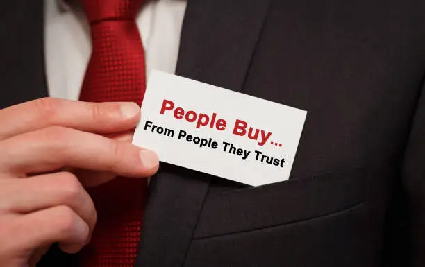 Photo of Businessman putting a card with text People Buy From People They Trust in the pocket