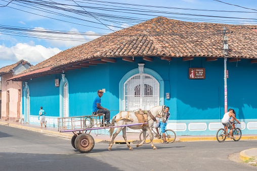Granada: People riding bicycles on the street of colorful commercial houses in the historic district of Granada in Nicaragua