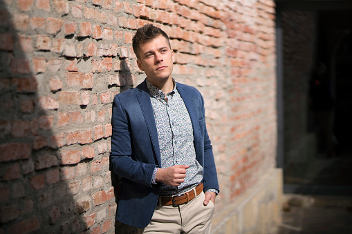 Fashion portrait of a handsome young man leaning on the brick wall.