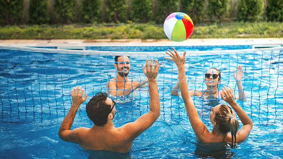 Closeup of group of young adults playing volleyball in a shallow swimming pool. There are two couple playing against each other.