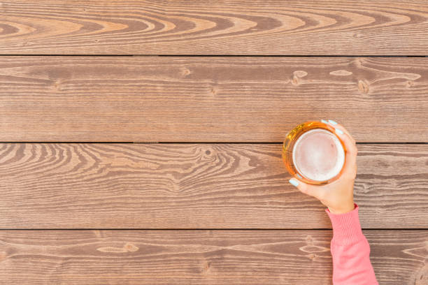 istock Female hand holding beer glass over wooden table 672157384