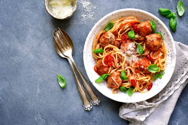 Spaghetti with meatballs in tomato sauce in a white craft bowl on a grey slate,stone or concrete background.Top view.