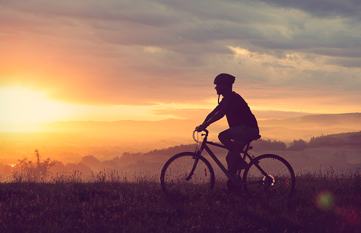 Cyclist going on bicycle in countryside in sunset light